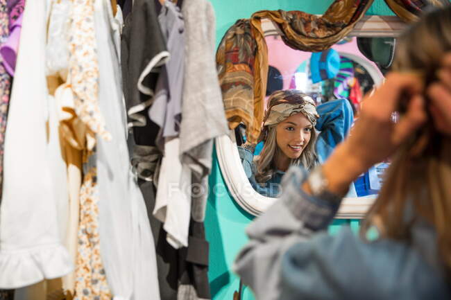 Зеркальное изображение молодой женщины, пытаясь на марочные одежду в магазине бережливость — стоковое фото