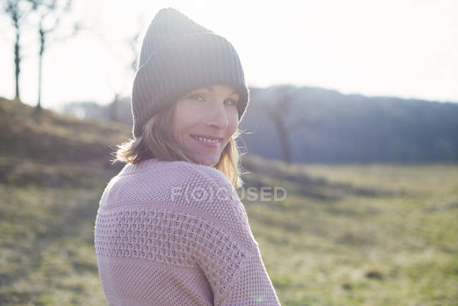 Retrato de mulher no campo iluminado pelo sol olhando por cima do ombro — Fotografia de Stock