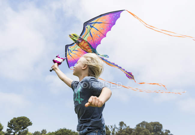 Menino correndo com pipa voadora contra o céu nublado — Fotografia de Stock