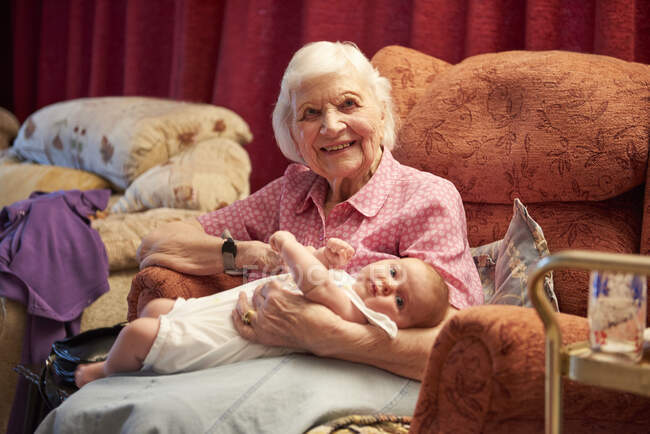Mulher sênior berço bebê bisneta na poltrona, retrato — Fotografia de Stock