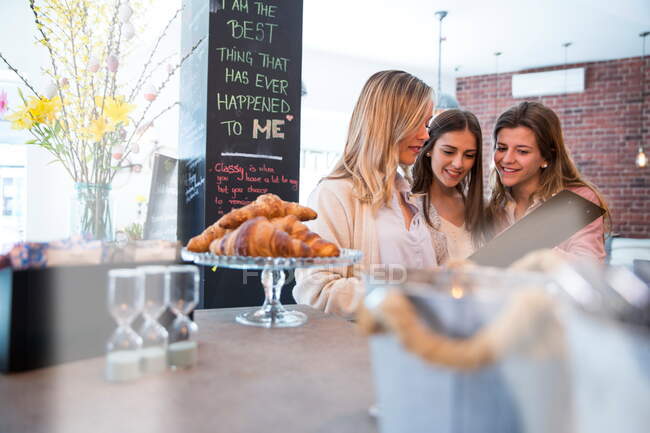 Drei Freundinnen schauen sich Speisekarte im Café an — Stockfoto
