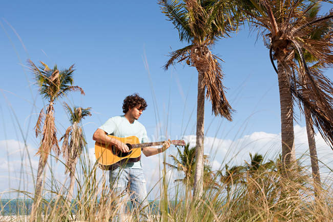 Young man playing guitar on beach — Stock Photo