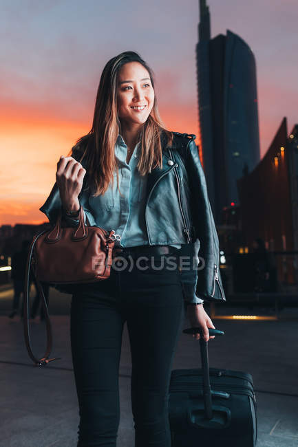 Donna d'affari che cammina con valigia a ruote all'aperto al tramonto — Foto stock