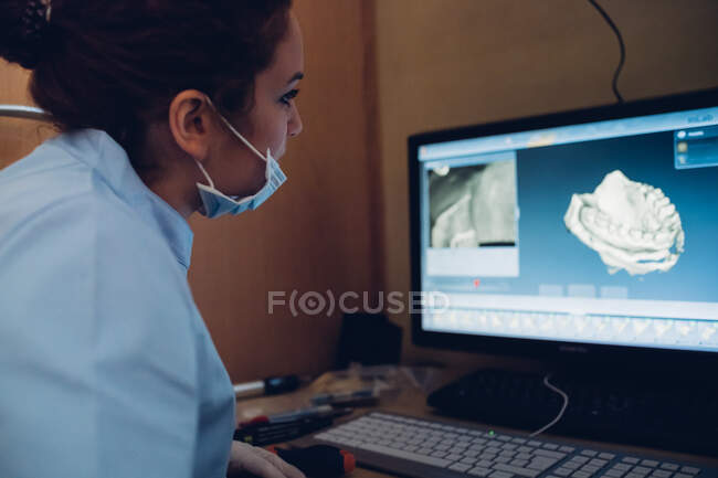 Жіночий стоматолог дивиться на модель зубів на екрані комп 