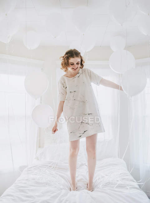 Woman jumping on bed and holding bunch of balloons — Stock Photo