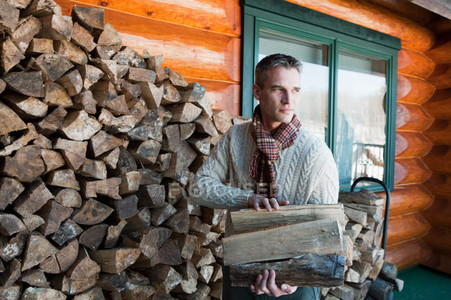 Portrait of man holding logs near house — Stock Photo