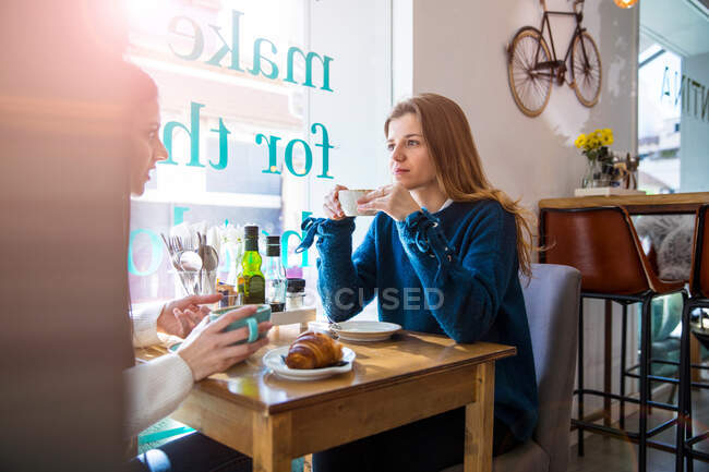 Dos amigas sentadas juntas en la cafetería, tomando café - foto de stock