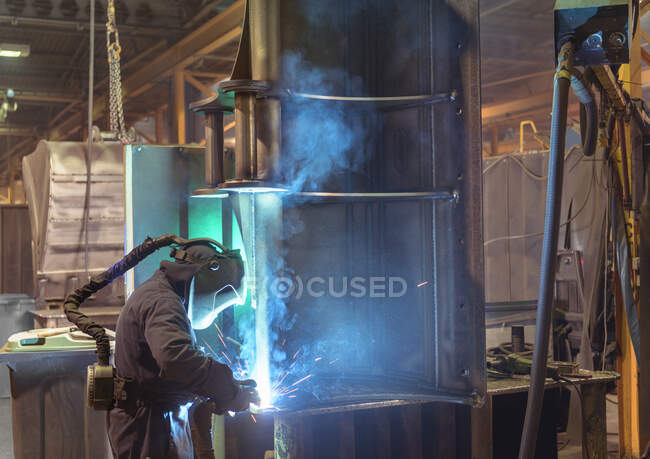 Welder welding part of digger bucket in engineering factory — Stock Photo