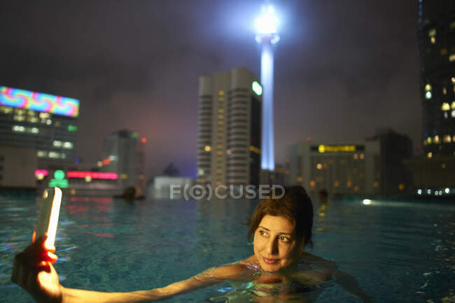 Tourist taking selfie in rooftop pool, KL Tower in background, Kuala Lumpur, Malaysia — Stock Photo
