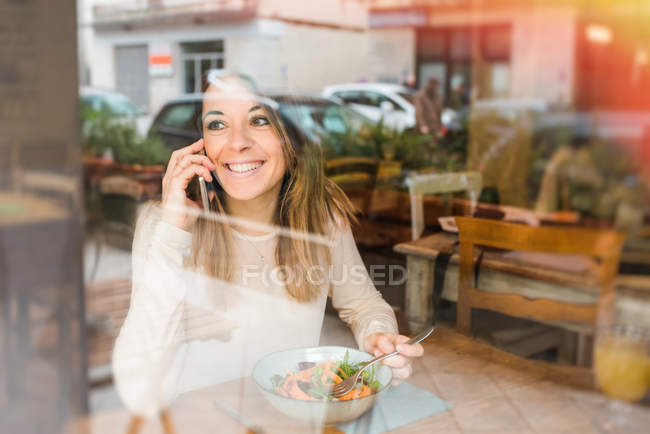 Woman talking on mobile phone while having meal in restaurant — Stock Photo