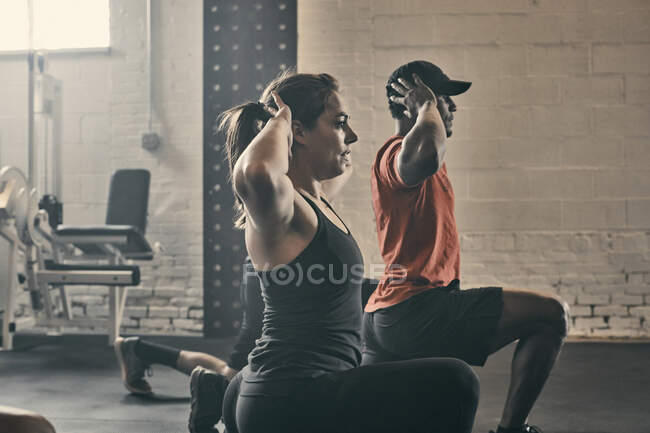 People exercising in gym, hands behind head lunging — Stock Photo
