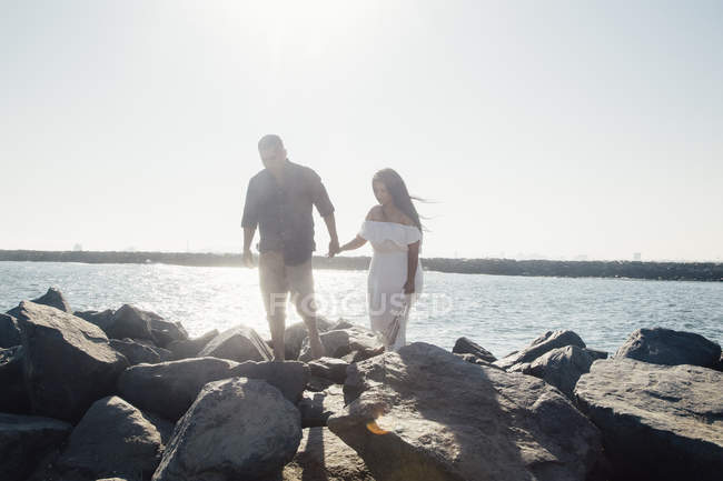 Casal andando sobre rochas costeiras, de mãos dadas — Fotografia de Stock