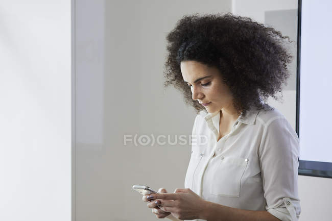 Jeune femme d'affaires au bureau textos sur smartphone — Photo de stock