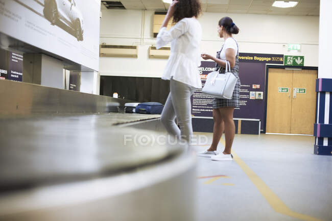 Friends waiting for suitcase by carousel in airport — Stock Photo