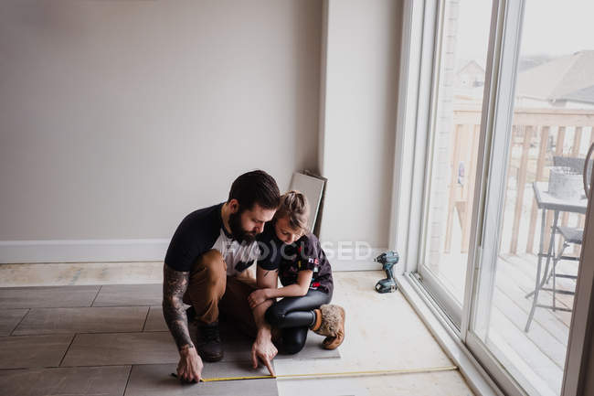 Девушка помогает отцу устанавливать плитку для пола — стоковое фото