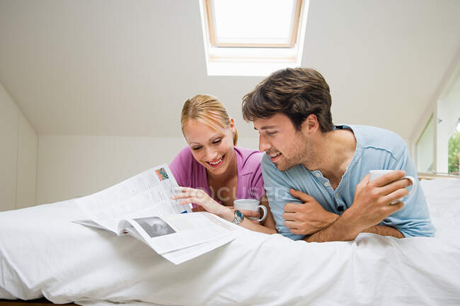 Молодая пара читает журнал на кровати — стоковое фото