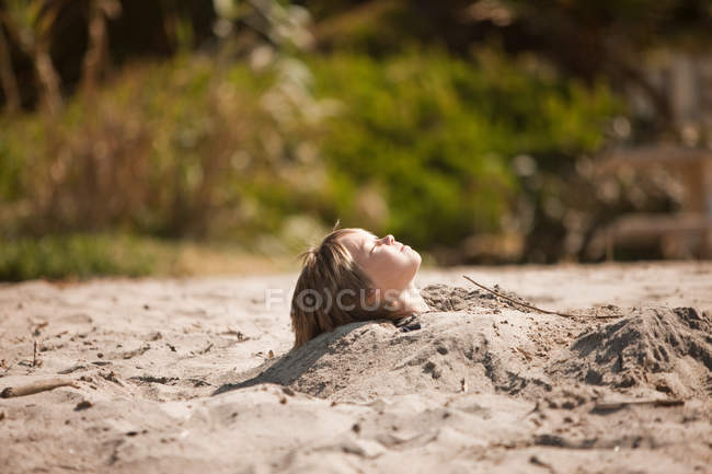 Seitenansicht eines Jungen, der bis zum Hals in Sand versunken ist — Stockfoto
