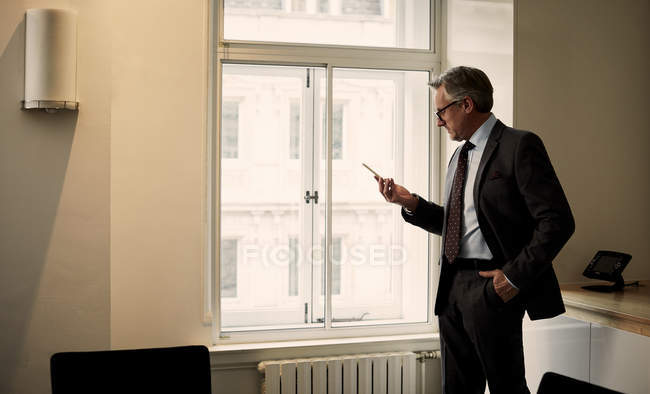 Зрелый бизнесмен в офисе пишет смс на смартфоне — стоковое фото