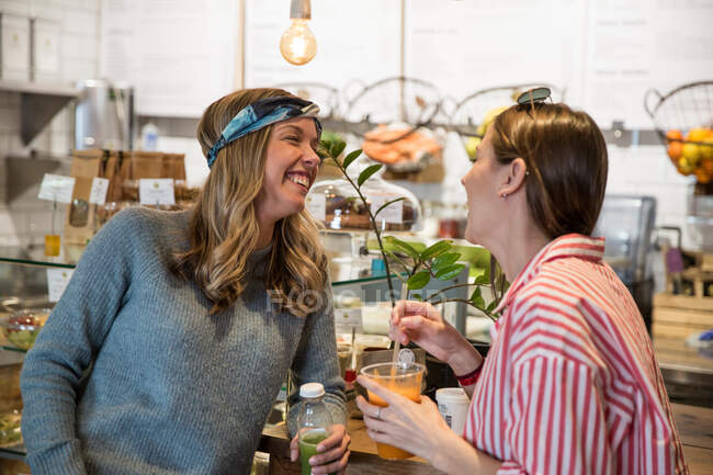 Dos amigas jóvenes riendo juntas en la cafetería - foto de stock