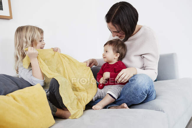 Famille assise sur le canapé, jeune fille jouant peek-a-boo avec la petite soeur — Photo de stock