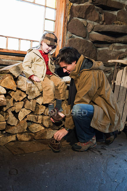 Padre mettere le scarpe su figlio in casa rustica — Foto stock