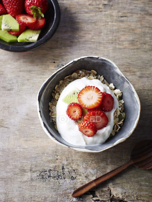 Bowl of muesli with strawberries and yogurt on wooden desk — Stock Photo