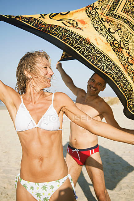 Pareja madura en playa sosteniendo manta de playa - foto de stock