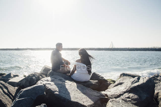 Casal sentado em rochas costeiras, olhando para a vista, visão traseira — Fotografia de Stock