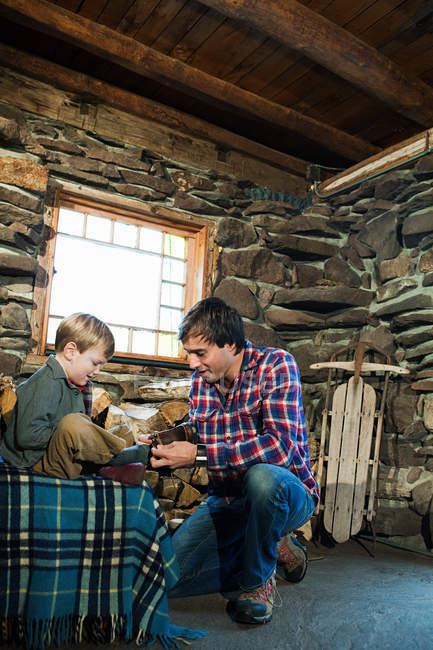 Father putting shoes on son in rustic house — Stock Photo