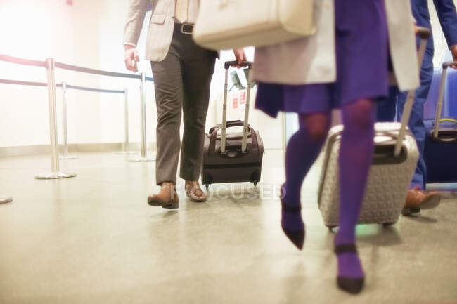 Бізнесмени та жінки в аеропорту, тягнуть колісні валізи, низька секція — стокове фото