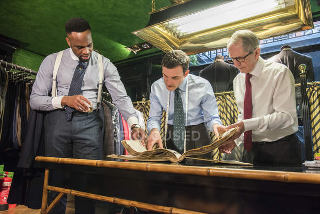 Tailors and customer looking at handmade swatch book in traditional tailors shop — Stock Photo