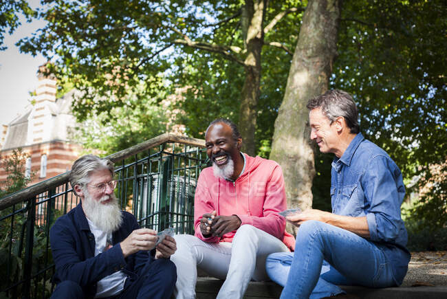 Three mature men, outdoors, sitting on steps, playing cards — Stock Photo