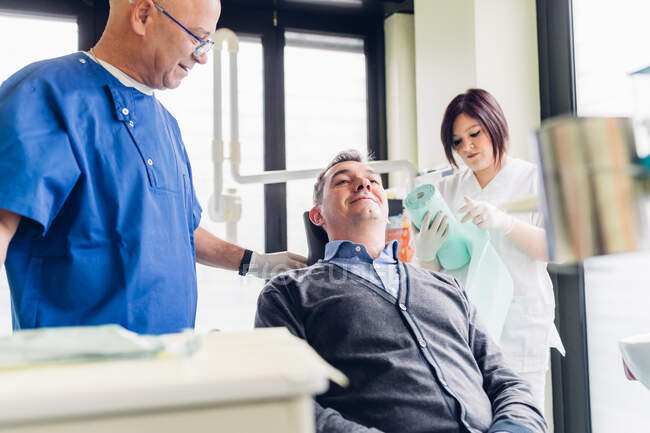 Paciente do sexo masculino em cadeira de dentista, dentista de pé ao lado dele — Fotografia de Stock
