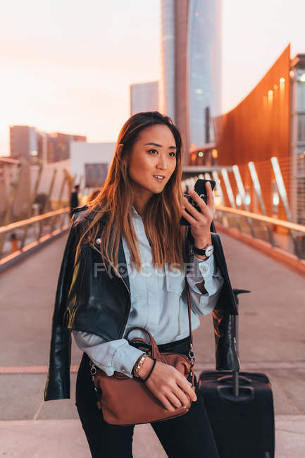 Mujer joven con maleta de ruedas usando smartphone - foto de stock