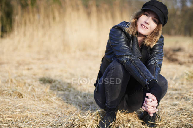 Woman in cap crouching on field straw — Stock Photo