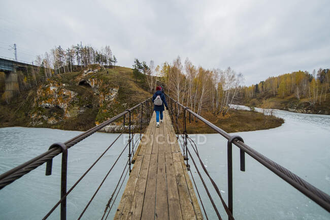 Вид сзади небольшой группы туристов, идущих по пешеходному мосту через реку, Кисловодск, Эвенк, Россия — стоковое фото
