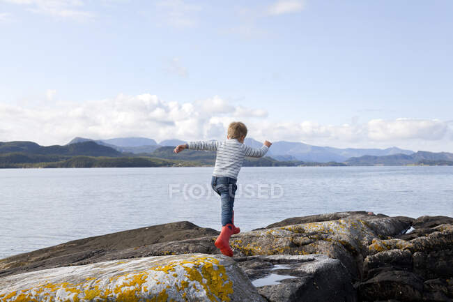 Boy jumping rocks by fjord, Aure, More og Romsdal, Noruega - foto de stock