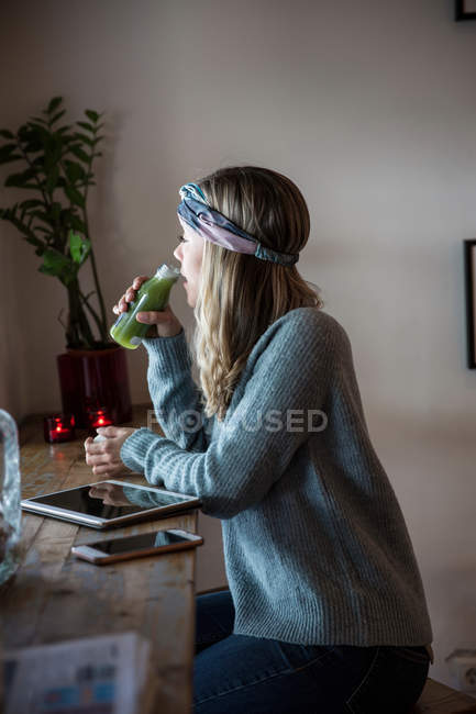 Side view of Young woman drinking vegetable juice at cafe window seat — Stock Photo