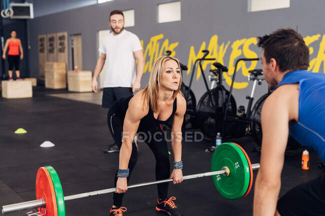 Homme et femme dans la salle de gym avec haltérophilie des haltères — Photo de stock