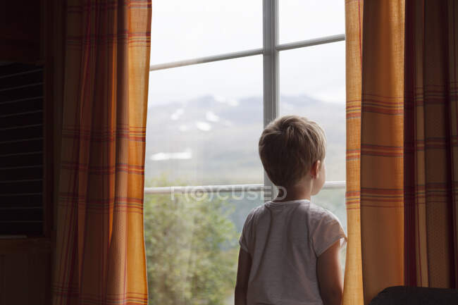 Мальчик смотрит через занавесное окно — стоковое фото
