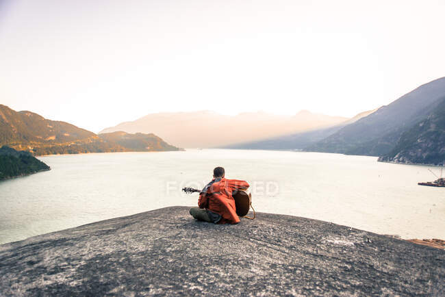 Jovem sentado no Malamute, tocando guitarra, visão traseira, Squamish, Canadá — Fotografia de Stock