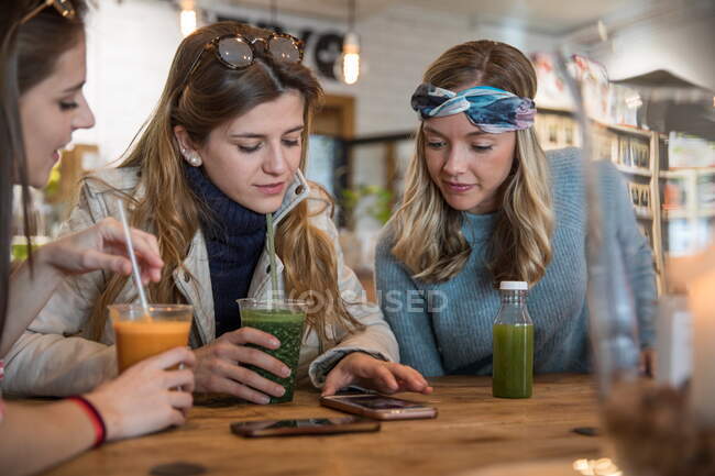 Três amigas, sentadas no café, a beber batidos, a rir — Fotografia de Stock