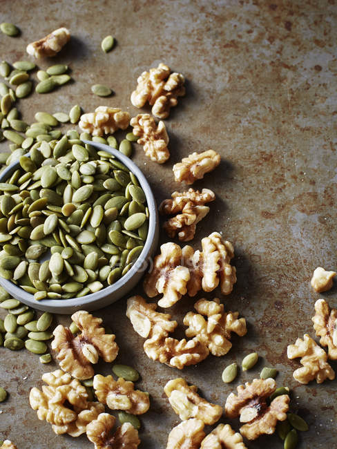 Still life with bowl of pumpkin seeds and walnuts, overhead view — Stock Photo