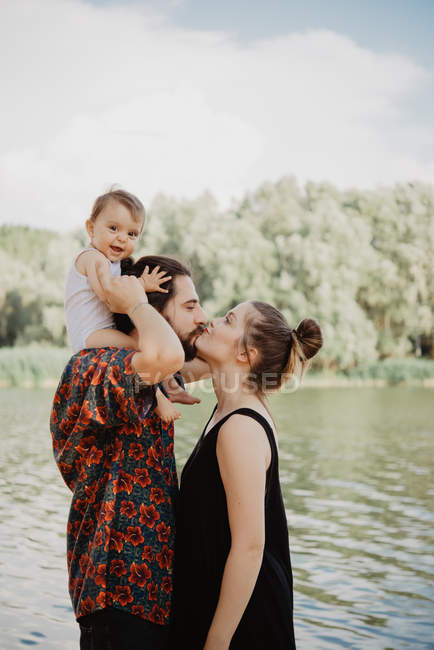 Casal com bebê menina beijando por lago, Toscana, Itália — Fotografia de Stock