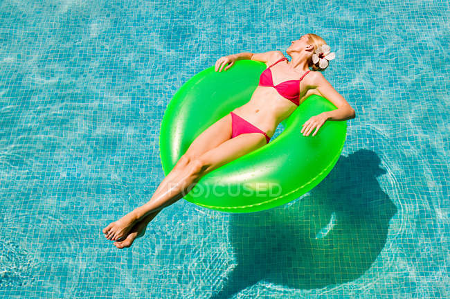 Молодая женщина, плавающая на зеленом надувном кольце в бассейне — стоковое фото