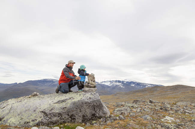 Caminhante masculino com filho construindo cairn na paisagem montanhosa, Parque Nacional Jotunheimen, Lom, Oppland, Noruega — Fotografia de Stock