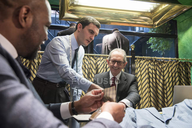Tailors and customer looking at swatches in traditional tailor shop — Stock Photo