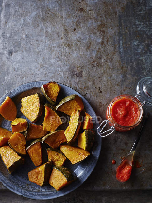 Still life of baked pumpkin on plate with jar of chilli sauce, overhead view — Stock Photo