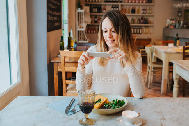 Woman taking photo of meal in restaurant — Stock Photo