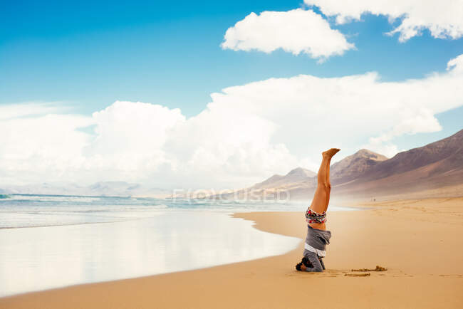 Женщина делает стойку на голове на пляже, Корралехо, Фуэртевентура, Канарские острова — стоковое фото